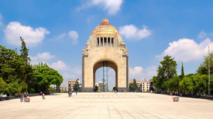 An arch-shaped monument with a gold dome on the top, next to trees and a cement path