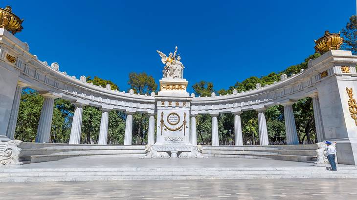 A large semi-circle white stone monument with arches and gold statues on top of it