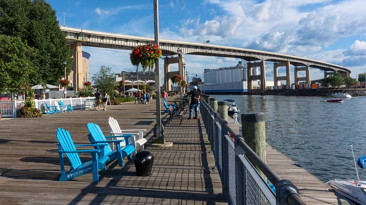 A walkway with blue chairs next to trees, a bridge, and a river