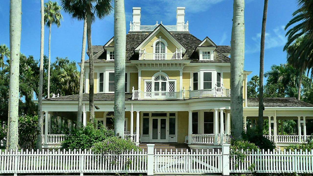 A fenced Georgian-Revival-style house surrounded by palm trees