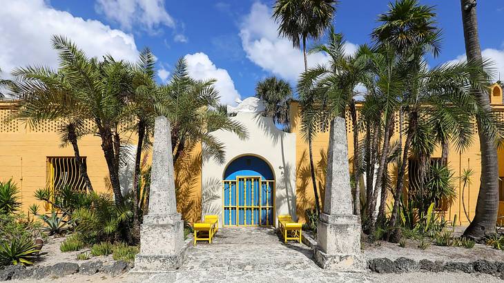 A stone building with yellow walls next to a path and palm trees