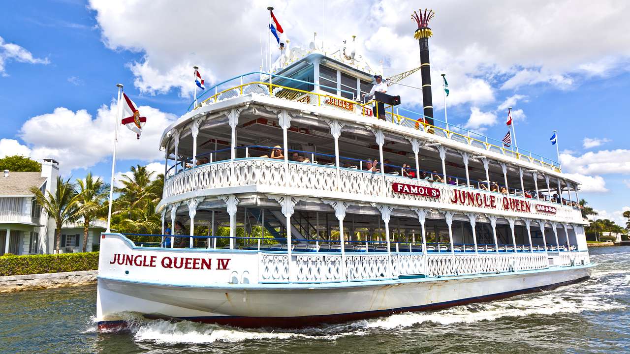 A white riverboat with a "Jungle Queen" sign and multiple flags on the water