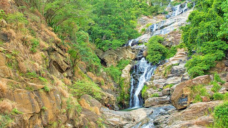 A waterfall flowing down a rocky track with a green trees around