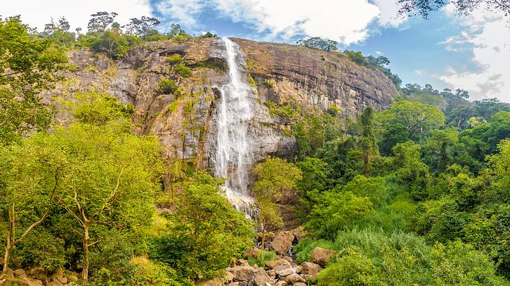 Water flowing down a rocky cliff with a few trees, and a partly cloudy sky above