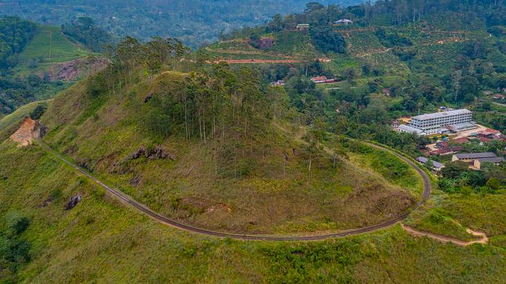 A green valley with a railway encircling one of the peaks, and a few buildings