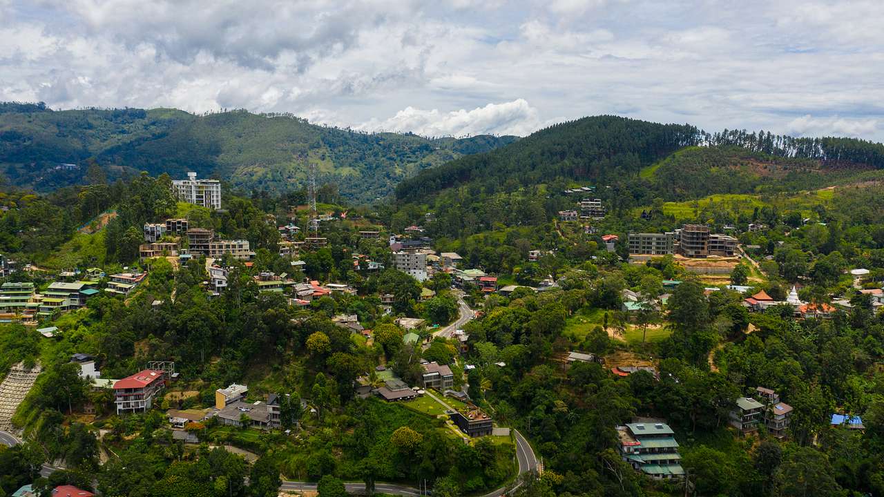 Aerial view of a city with buildings, trees, mountains, and a cloudy sky