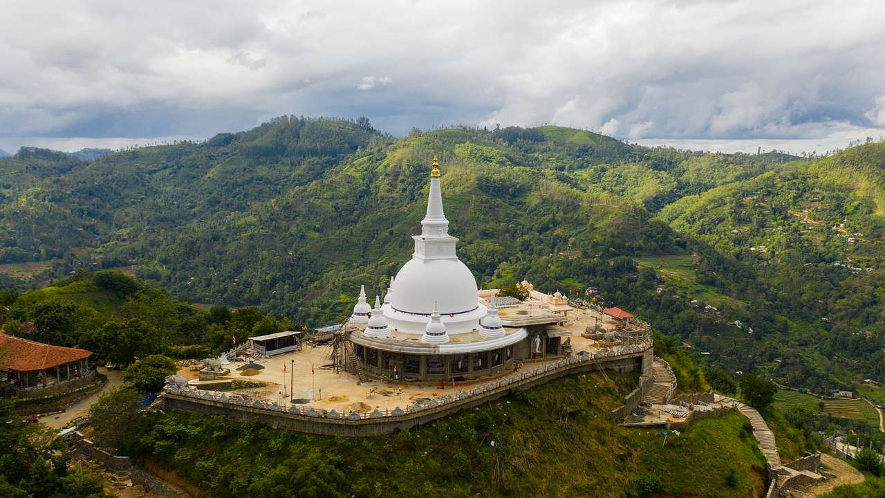A religious structure on a hilltop surrounded by green mountains, and a cloudy sky