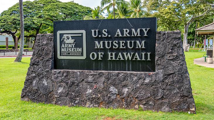 A sign on a stone base that reads "U.S. Army Museum of Hawaii", and trees at the back