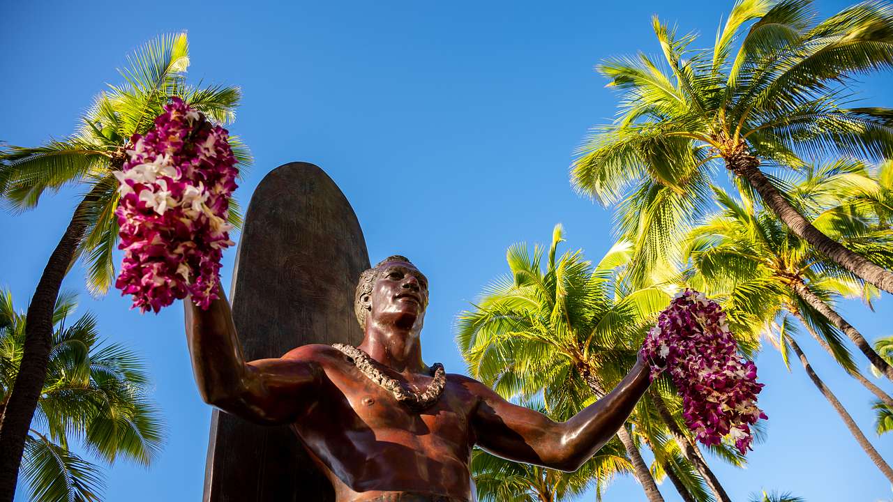 A statue of a man holding flower bunches in each hand, with palm trees behind him