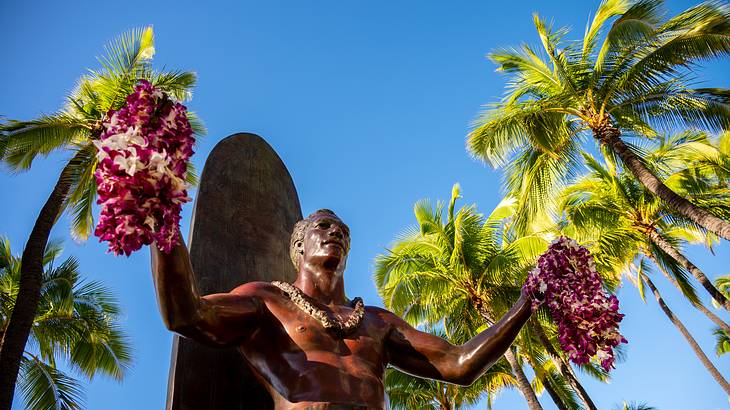 A statue of a man holding flower bunches in each hand, with palm trees behind him