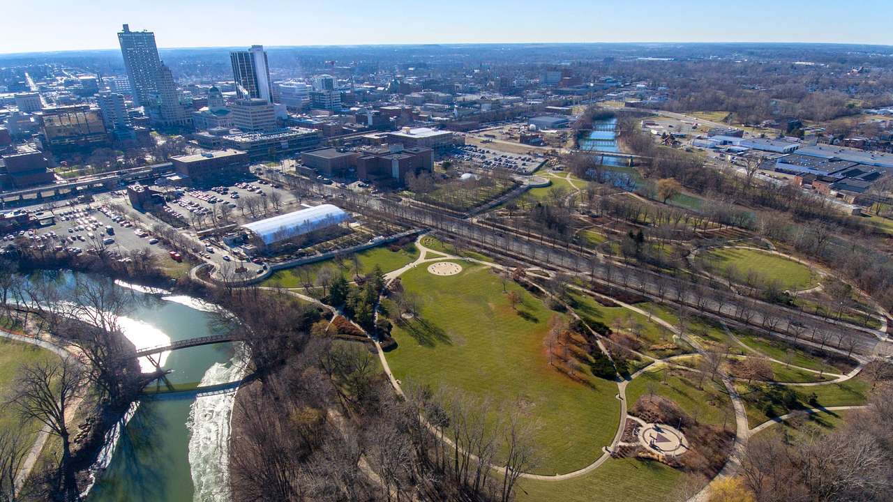 An aerial view of a park with bare winter trees next to a river and city buildings