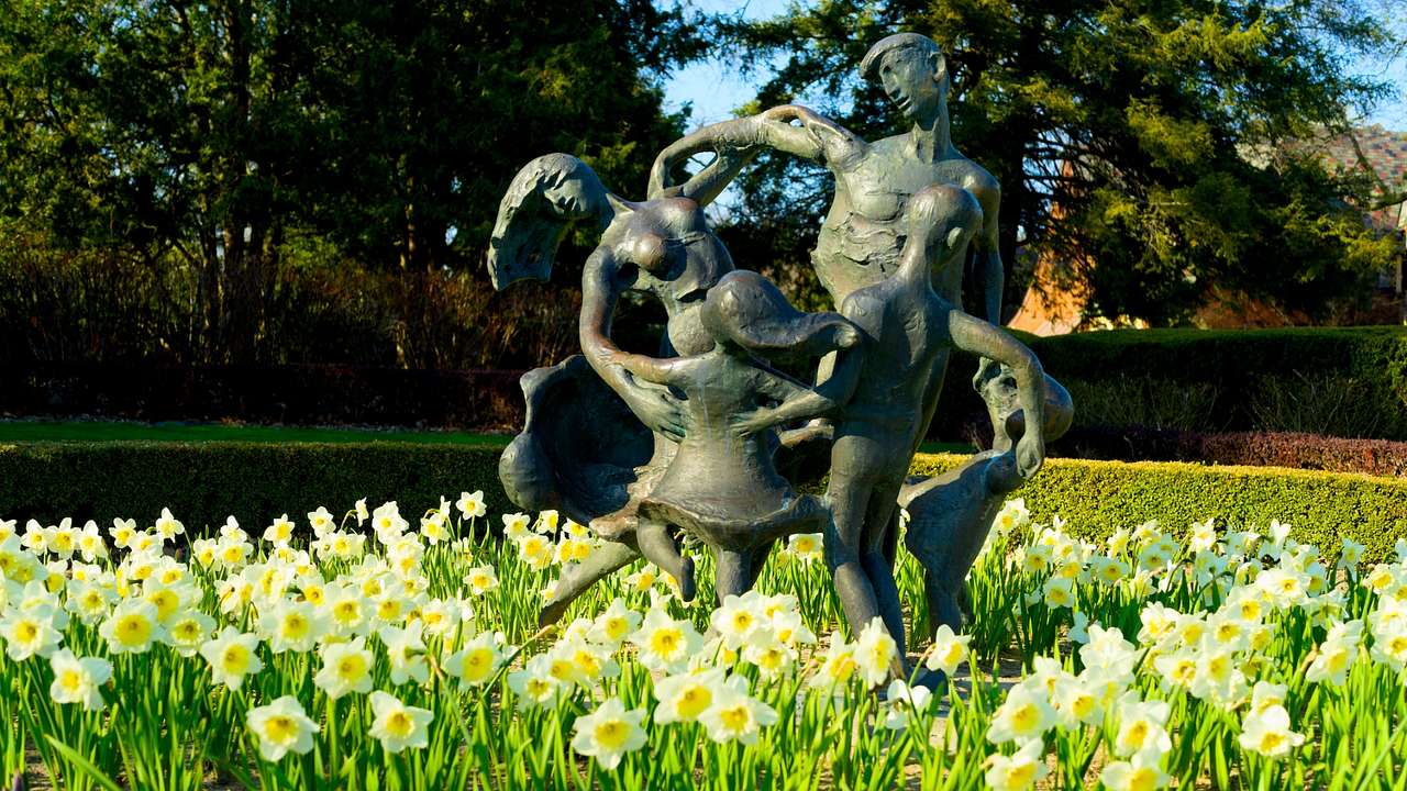 A statue of people dancing in a daffodil garden with trees in the background