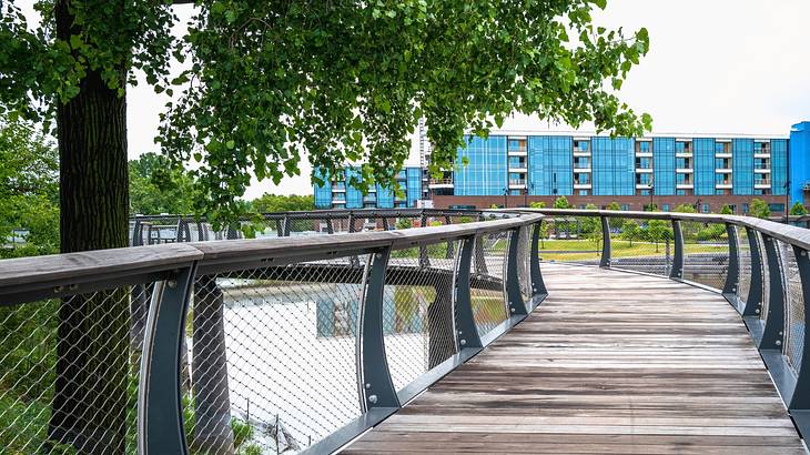 A wooden bridge next to trees, a river, and blue buildings