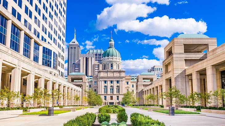 A path with greenery and buildings on either side next to a building with a dome