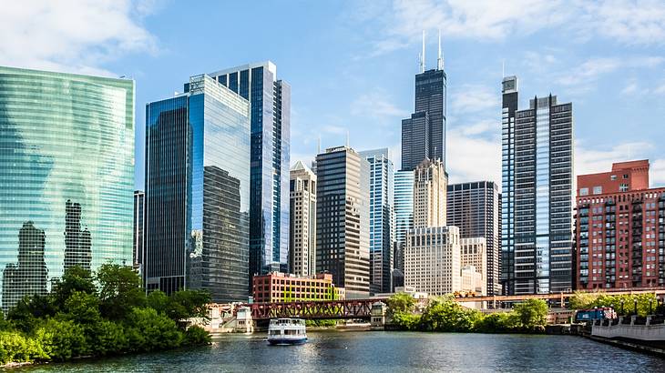 A city skyline with modern buildings next to greenery and a river with a boat on it