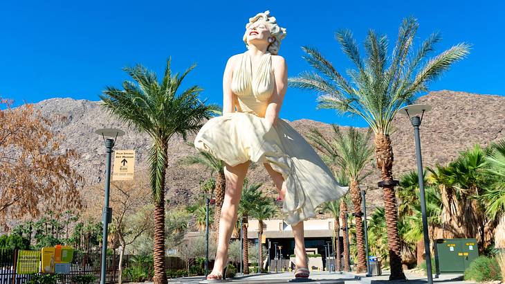 A statue of a woman in a white dress on a path lined with palm trees