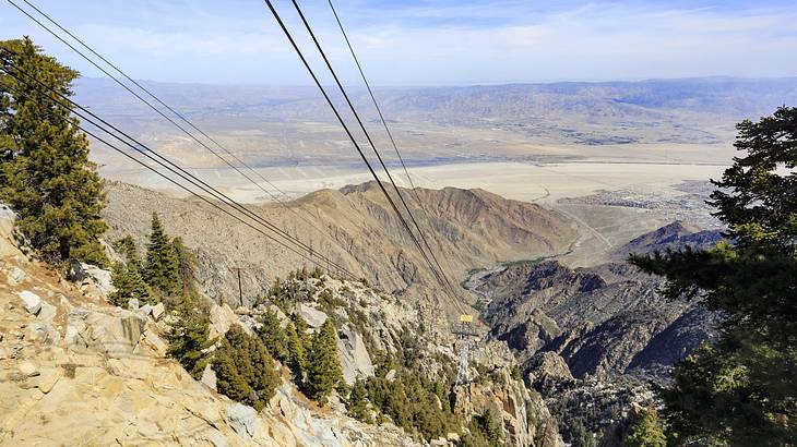 An aerial view over mountains with trees on them and a cable car line