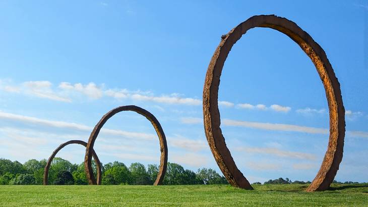 A set of three arch sculptures on the grass under a blue sky with some cloud