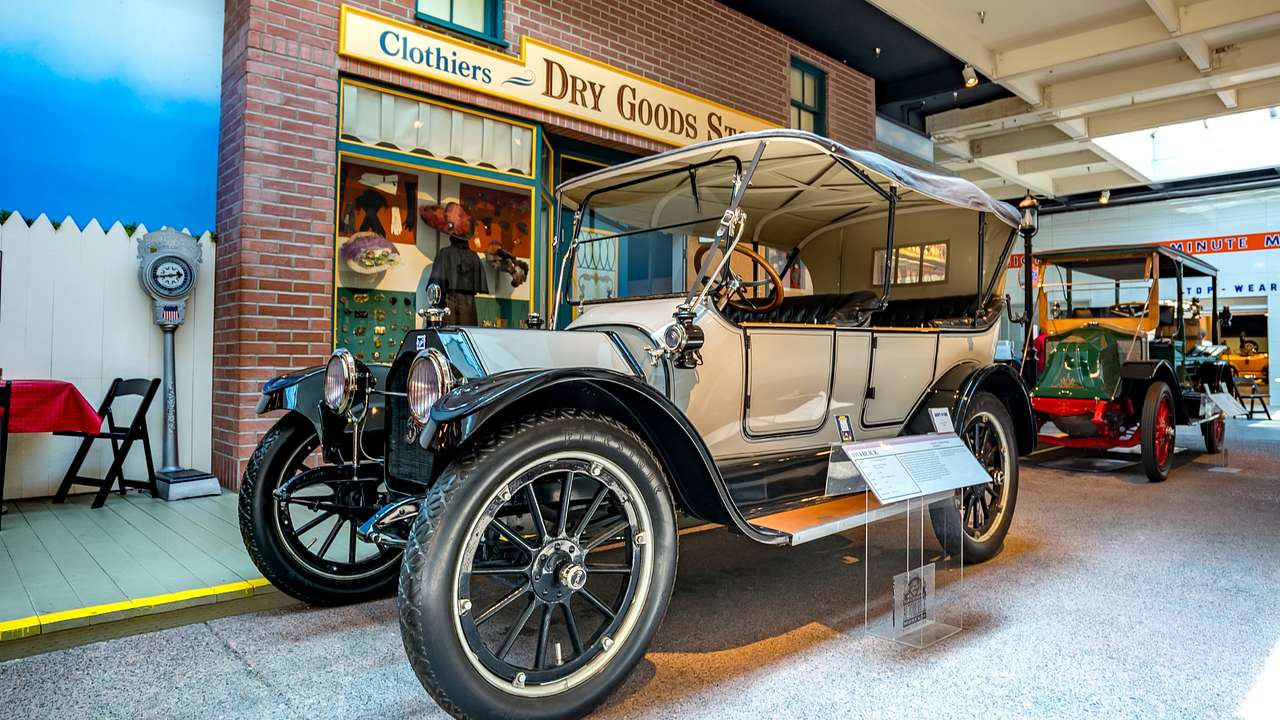 A vintage car in a museum next to a replica of an old-fashioned store