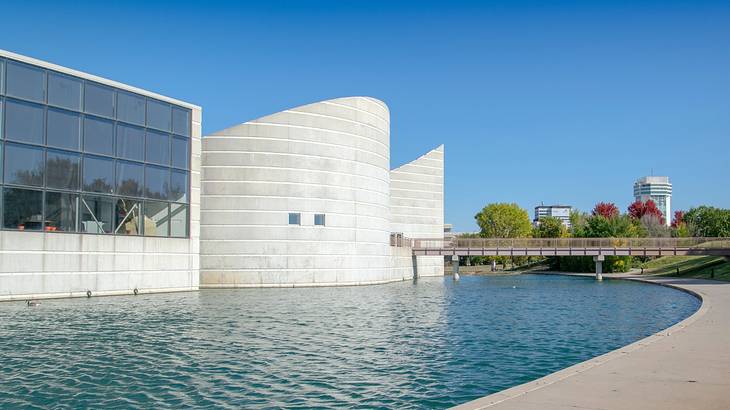 A rotunda next to a building with a large glass window, a pond, and a bridge