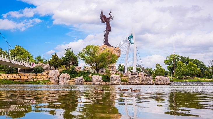 A body of water next to trees, a bridge, and a statue