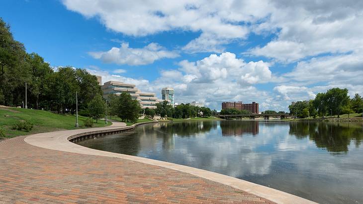 A river next to a brick path and trees under a blue sky with clouds