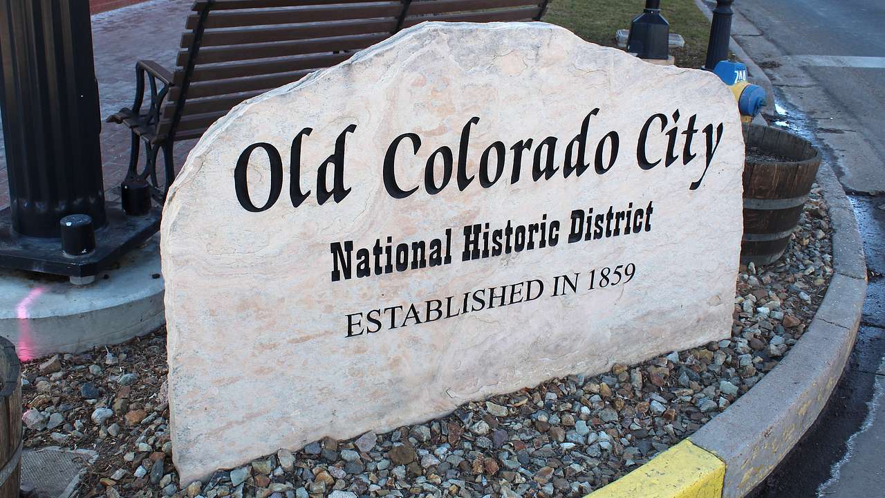 A stone slab that says "Old Colorado City" on a street corner with a bench behind it