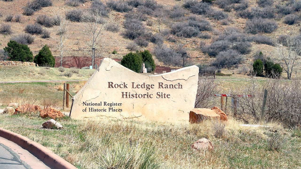 An irregularly-shaped stone sign on grassy ground saying "Rock Ledge Historic Site"