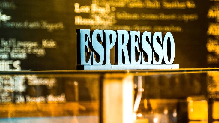 A white sign that says "Espresso" on a glass display case in a coffee shop