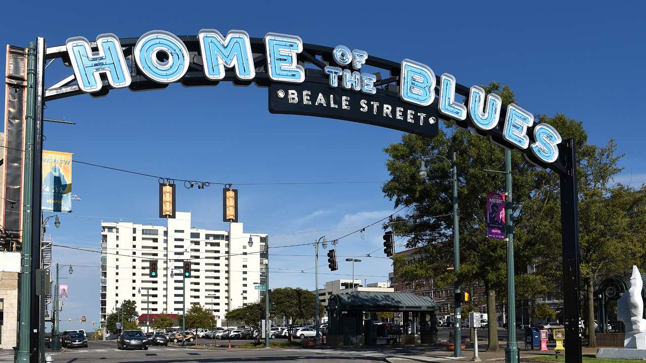 A street with a large sign over it saying "Home of the Blues," with buildings behind