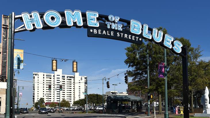 A street with a large sign over it saying "Home of the Blues," with buildings behind