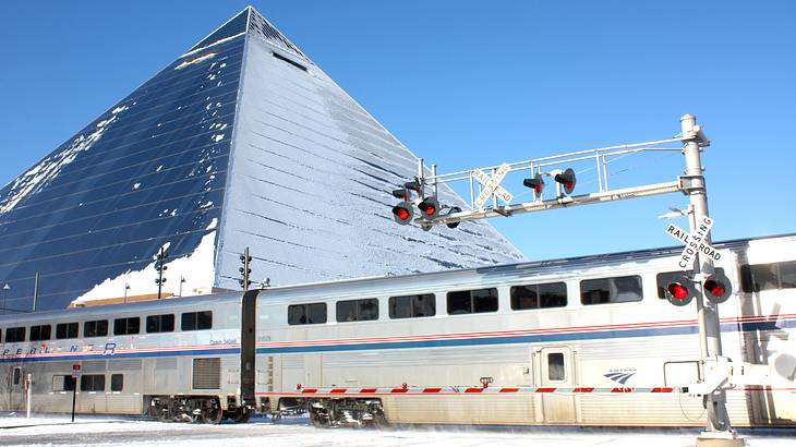 A train passing by a large shiny pyramid with a light covering of snow