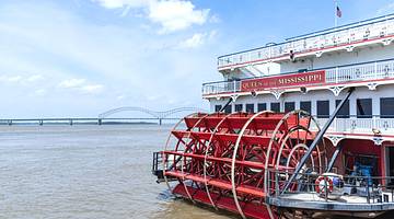 An old-fashioned white and red paddlewheel boat on a river near a bridge