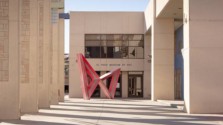 A red sculpture of two connected triangles in front of a building
