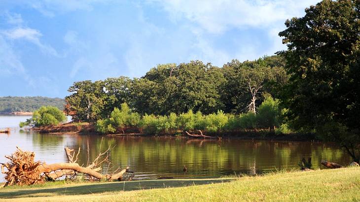 A lake against a cove covered with trees under a partly cloudy sky