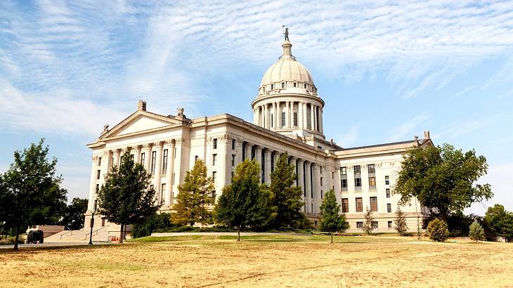 A white capitol building with columns and a dome, and some trees outside of it