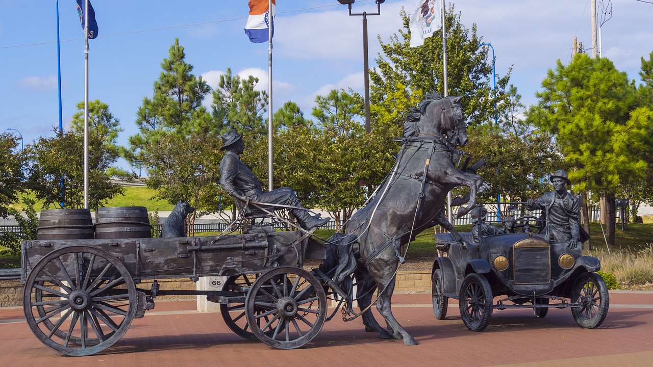 Bronze sculptures of a horse-drawn carriage and an old automobile in a square