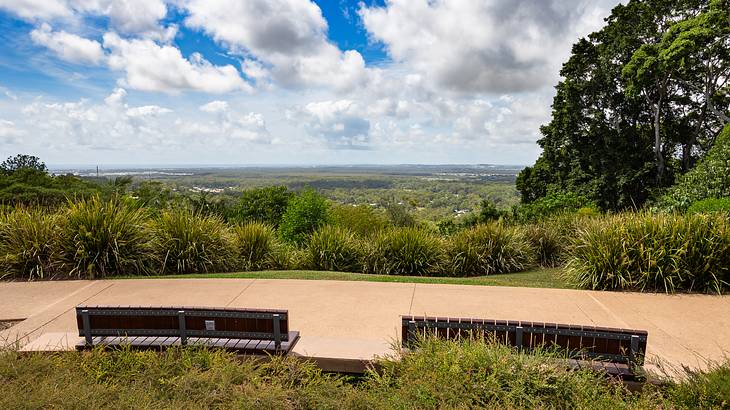 Two benches along paved cement overlooking a green landscape