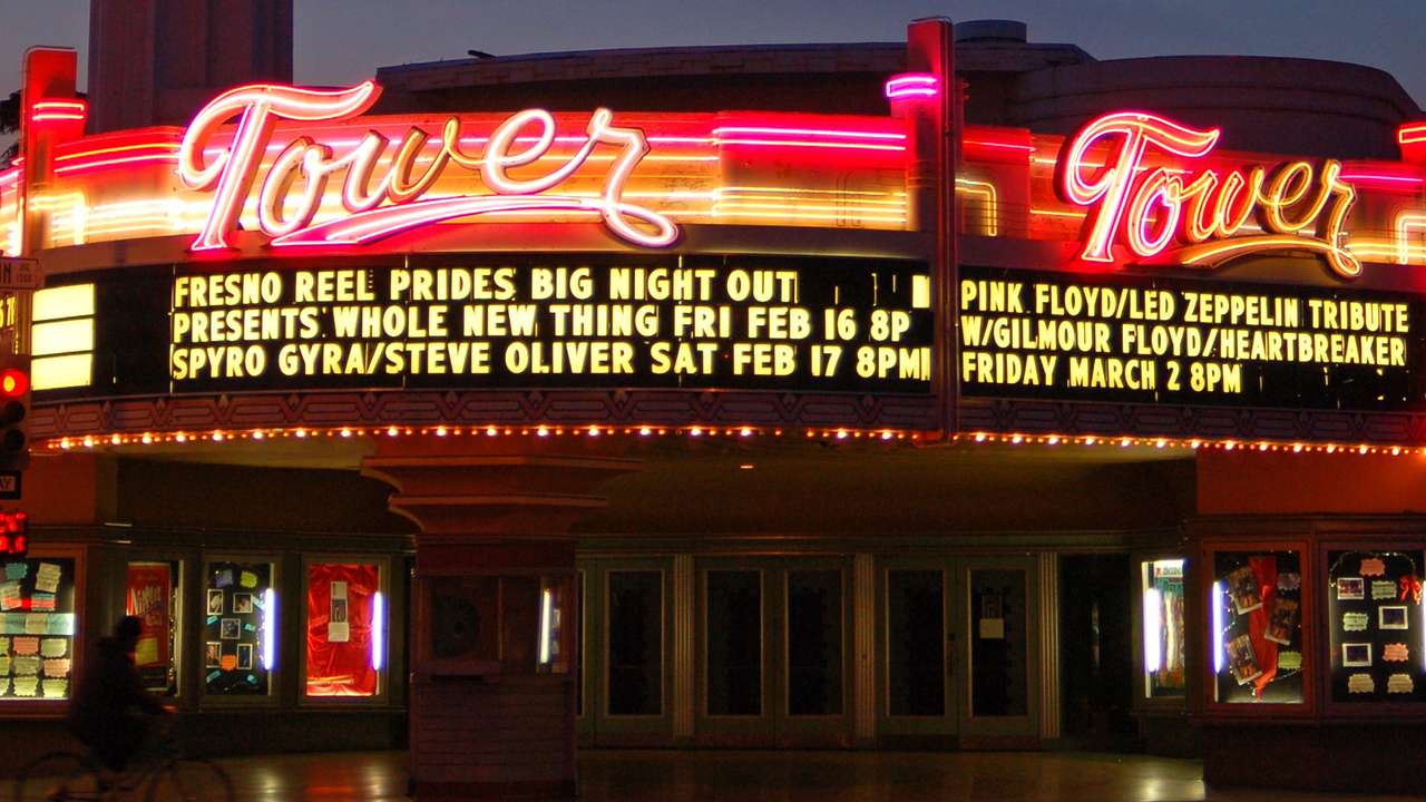 The illuminated exterior of a theater at night with a sign that says "Tower"