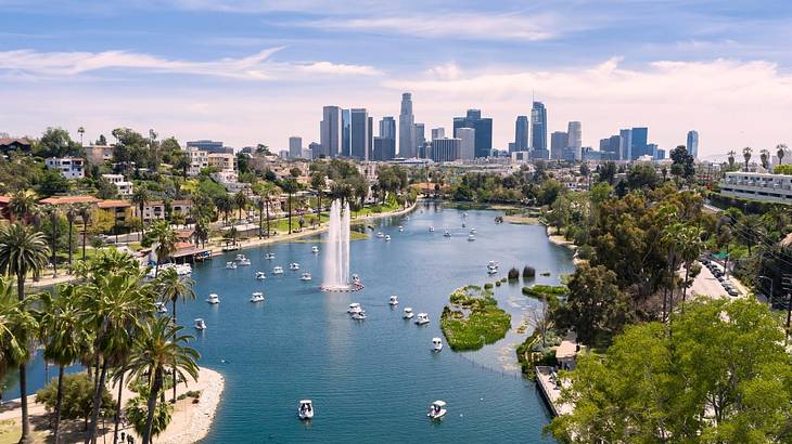 A large pond with a water fountain surrounded by palm trees next to a city skyline