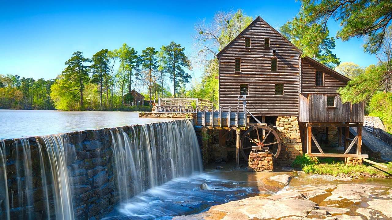 A wooden structure and mill with a waterfall in front of it and trees behind