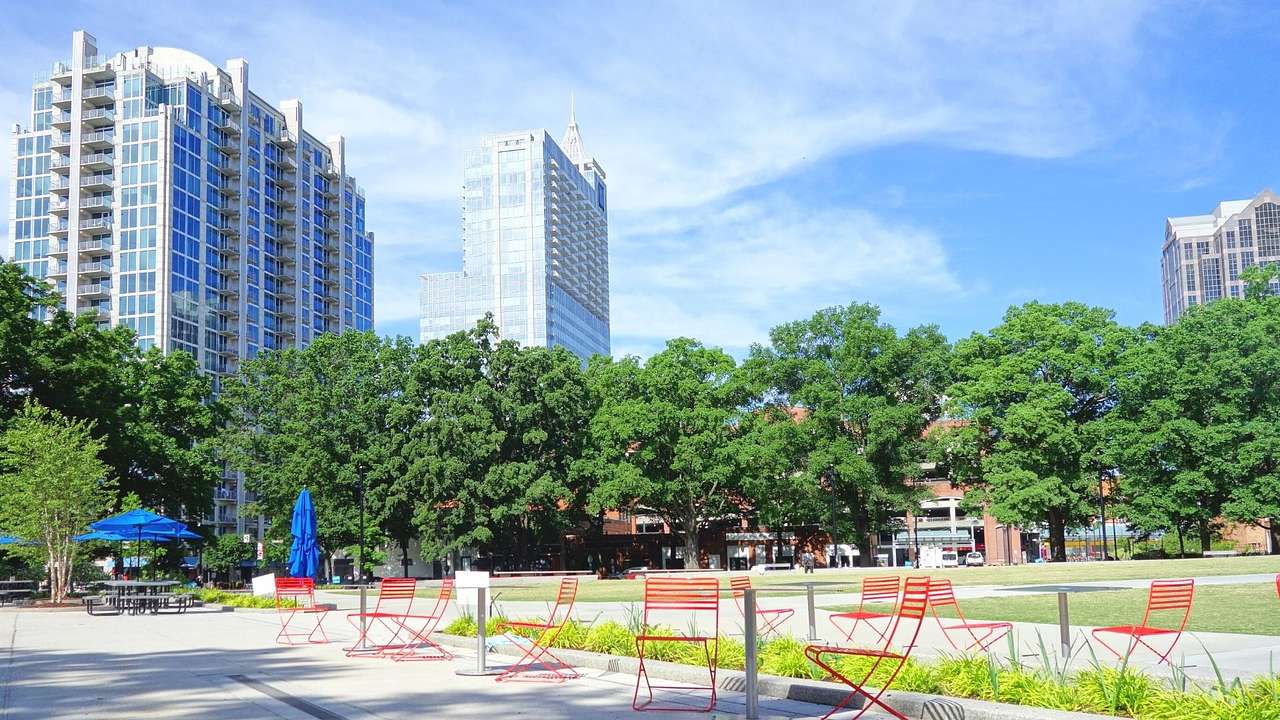 A green park and red chairs on a patio, and skyscrapers in the background