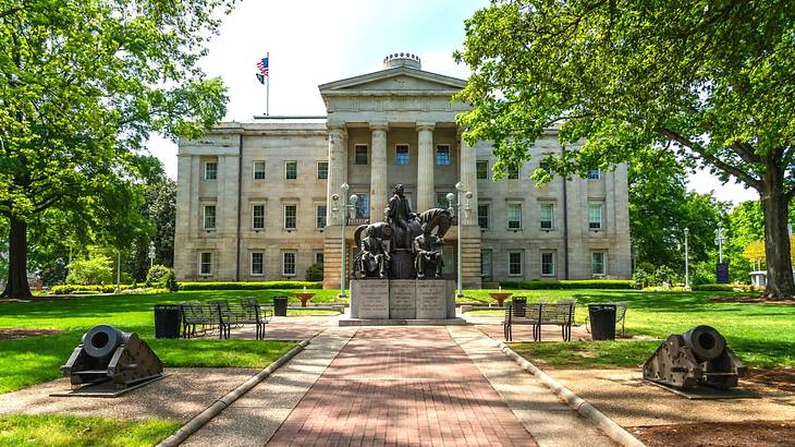 A stone building with columns and a statue, path, and trees in front of it