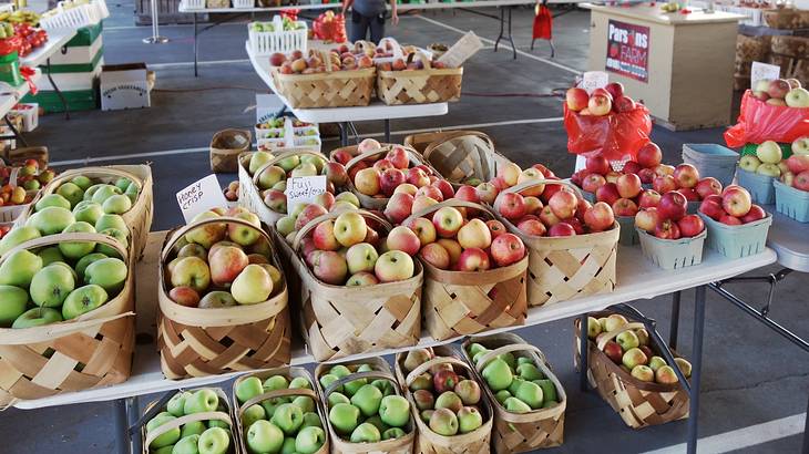 A table at a market with various types of apples in baskets