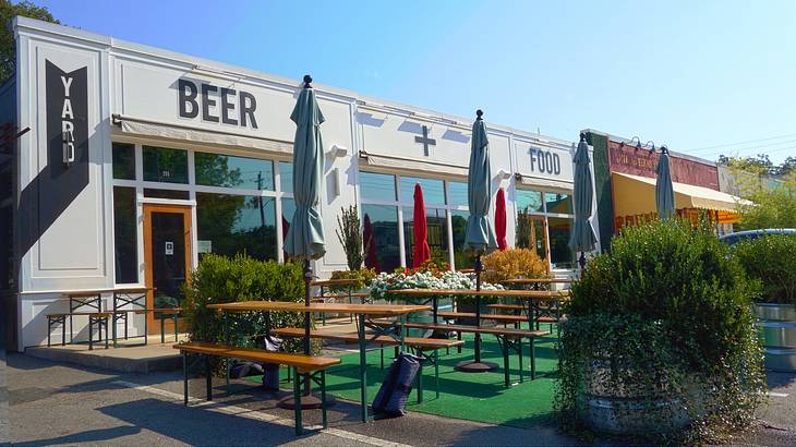 The front of a restaurant with a patio and a sign that says "Yard Beer + Food" The front of a restaurant with a patio and a sign that says "Yard Beer + Food"