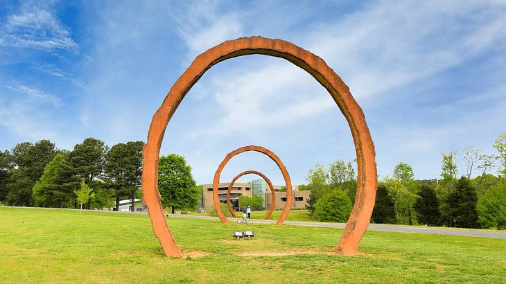 An art installation with three rings on the grass next to trees and a blue sky