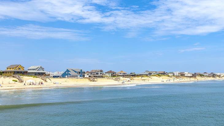 The ocean next to a sandy beach and small houses under a blue sky