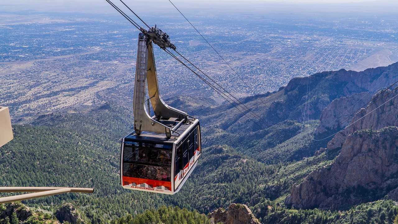 A cable car above greenery-covered mountains and a town in the distance