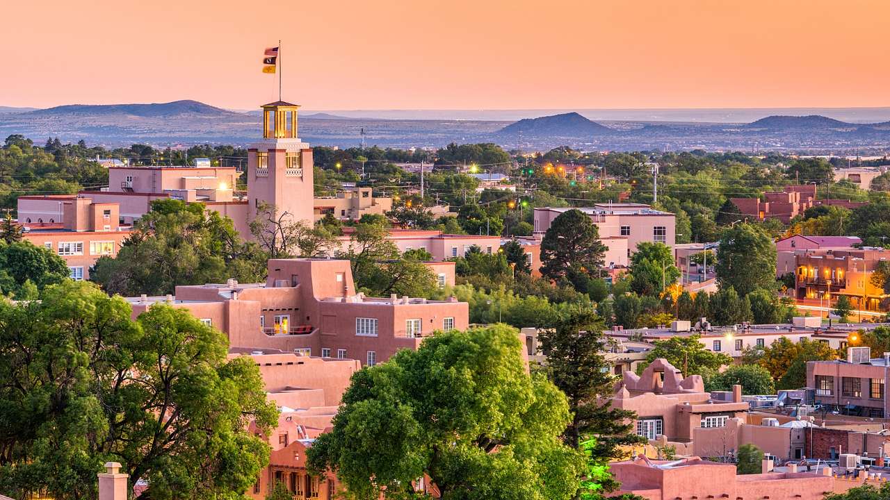 Pink stone buildings and a tower with a flag atop it surrounded by trees at sunset