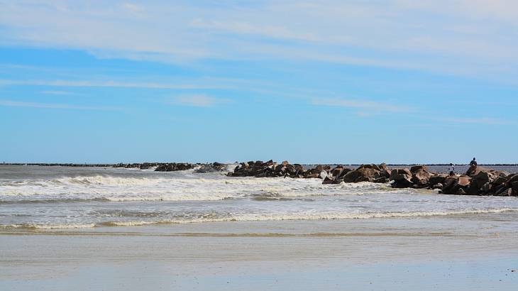 A beach with sand, ocean water, and rocks, under a blue sky A beach with sand, ocean water, and rocks, under a blue sky